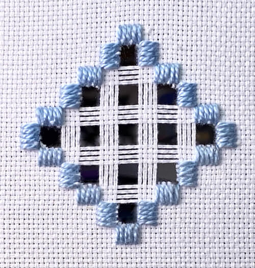 Hardanger embroidery sample showing cut threads removed to reveal openwork areas, surrounded by pale blue Kloster blocks and completed woven bars in white thread Hardanger embroidery sample showing cut threads removed to reveal openwork areas, surrounded by pale blue Kloster blocks and completed woven bars in white thread