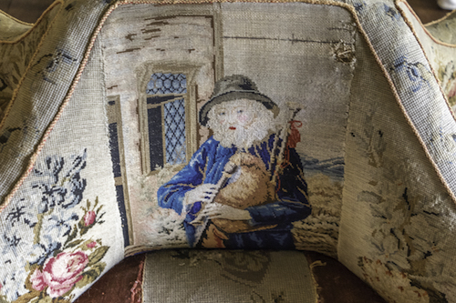 Close up of the Conversation Seat needlepoint showing an old man playing the Border Pipes