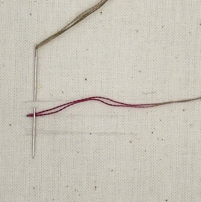 Cretan stitch step 1 — bringing the needle up on the middle line and making the first half of the stitch