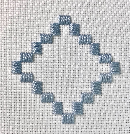 Hardanger embroidery sample showing Kloster blocks arranged in a diamond pattern with blue pearl cotton on white fabric