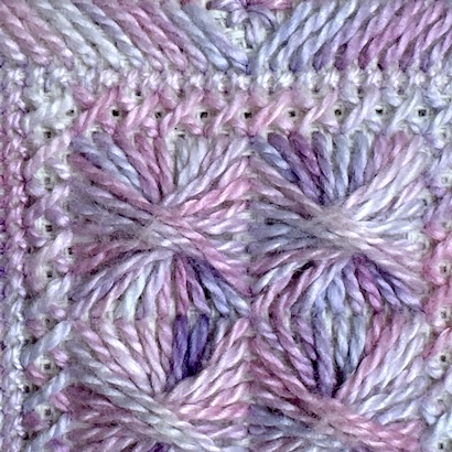 Close-up showing how over-dyed thread creates different colour effects in Rhodes stitch, cross stitch and gobelin — the same lavender thread pools and shifts differently in each stitch type